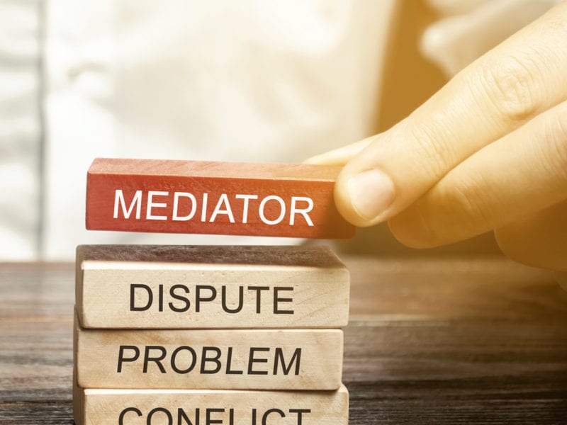 A man holds wooden blocks with the word Mediator, dispute, problem, conflict. Settlement of disputes by mediator. Dispute Resolution and Mediation. Third party, intermediary.