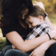 A Woman Putting Her Arms Around A Child Sitting On Her Lap